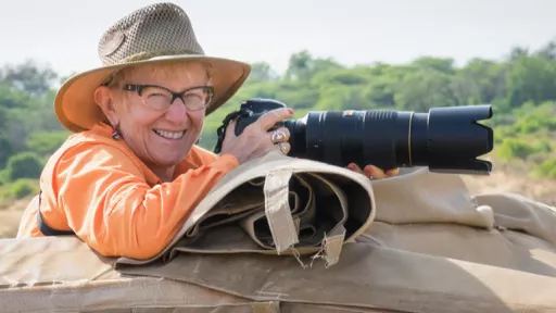 Woman using telephoto camera, lying on safari vehicle.