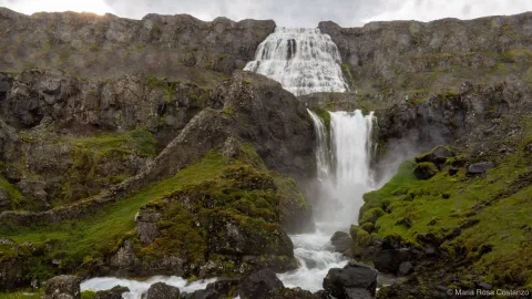 Waterfall cascading down rocky cliffs with green grass.
