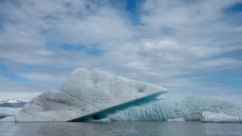 Floating iceberg under a cloudy sky in a calm body of water.
