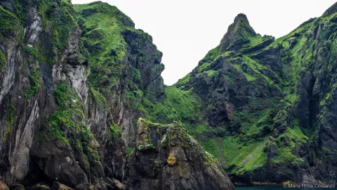 Steep green cliffs with rugged peaks against a cloudy sky.